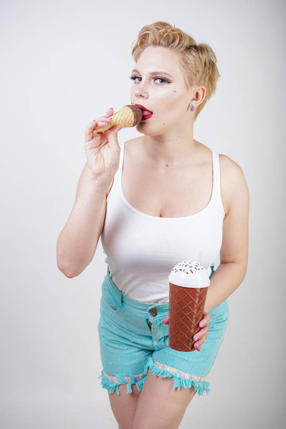 pretty caucasian blonde short hair girl eating tasty ice-cream with waffle cone and chocolate on white studio background - Фото, изображение
