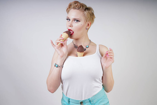 pretty caucasian blonde short hair girl eating tasty ice-cream with waffle cone and chocolate on white studio background - Fotó, kép