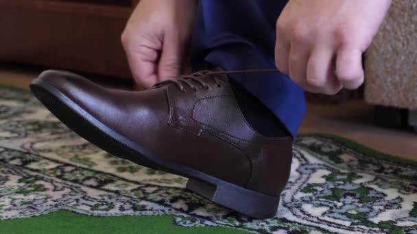 Mann bindet Schnürsenkel an braune Schuhe, ein Mann in weißem Hemd und dunkler Hose. Geschäftsmann zieht sich morgens zur Arbeit an. - Filmmaterial, Video