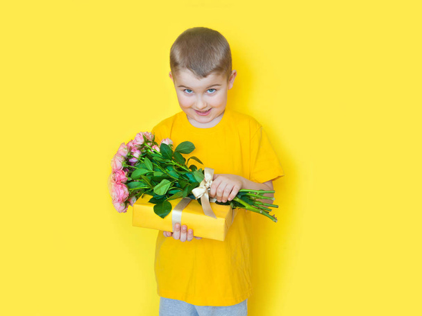 A boy in yellow clothes is holding a large bouquet of roses and  - Фото, изображение