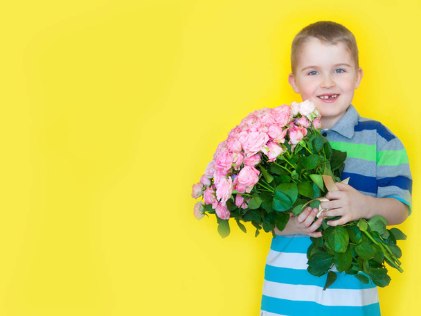 The boy is holding a large bouquet of roses and a gift. Yellow b - Фото, изображение