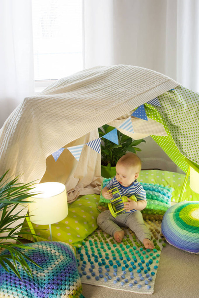 A little child toddler is sitting in a children's tent at home. - Zdjęcie, obraz