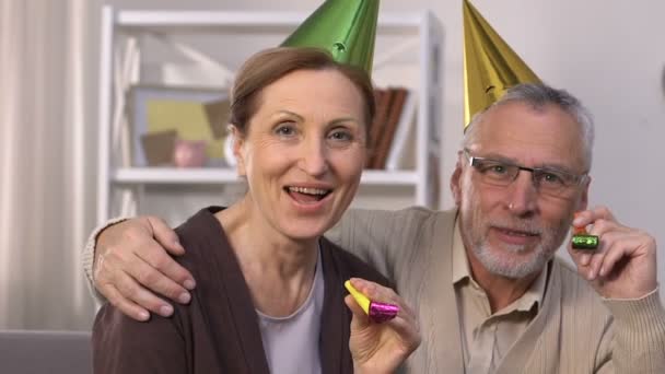 Cheerful senior couple in party hats celebrating birthday, making surprise - Video, Çekim