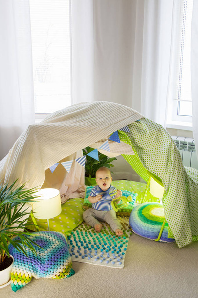 A little child toddler is sitting in a children's tent at home. - Photo, image