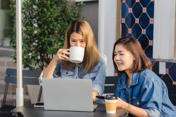 Aasian nuoret naiset älykkäissä rento vaatteet työskentelevät lähettämällä sähköpostia kannettavalla tietokoneella ja juomalla kahvia istuessaan kahvilassa. Elämäntapa naiset viestintä ja työskentely kahvilassa käsite
. - Valokuva, kuva