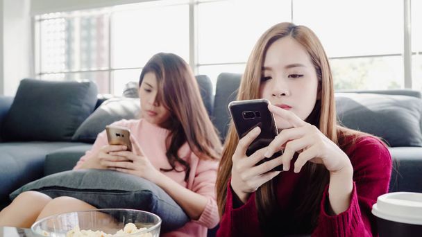 Aziatische vrouwen gebruik van smartphone en popcorn eten in de huiskamer, groep van kamergenoot vriend geniet van grappige moment liggend op de Bank. Levensstijl vrouwen ontspannen thuis concept. - Foto, afbeelding