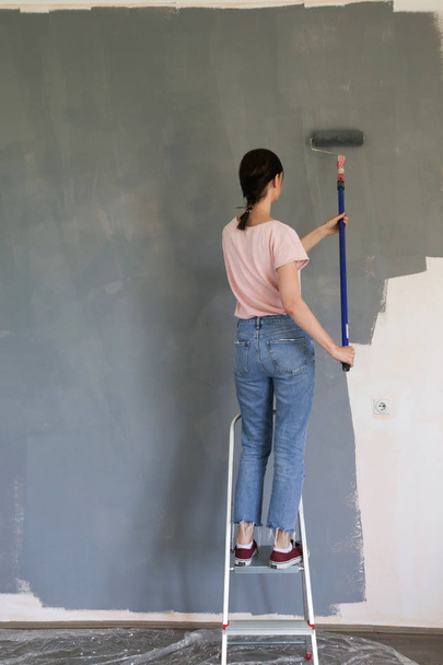 Γυναίκα ζωγραφική με γκρι χρώμα πάνω από ένα λευκό τοίχο - Φωτογραφία, εικόνα