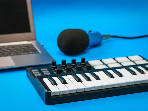 Musikmischpult, offenes Laptop und Mikrofon mit Drähten auf blauem Hintergrund. - Foto, Bild