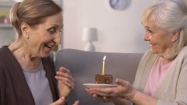 Seniorin schenkt Freundin Geburtstagstorte, Dame macht Wünsche und bläst Kerze - Filmmaterial, Video