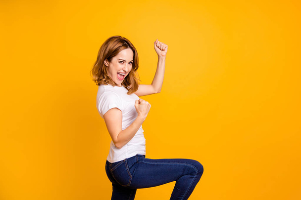 Портрет милої чарівної прекрасної леді кричати так шанувальник удачі святкувати вміст задоволений підняти кулаки руки одягнені сучасні джинсові джинси одяг ізольований жовтий фон
 - Фото, зображення