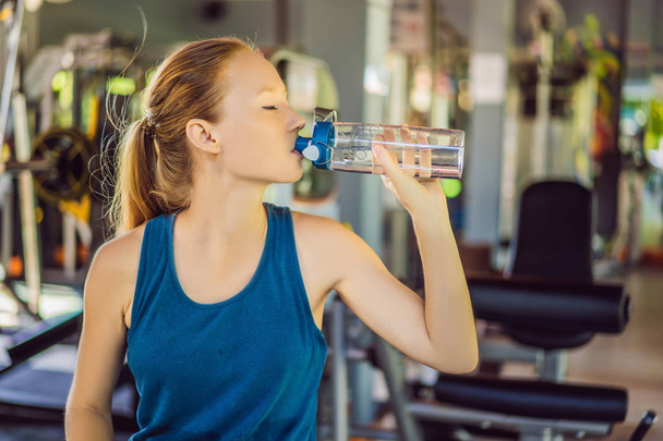 Young athletic woman drinking water in gym - Фото, зображення