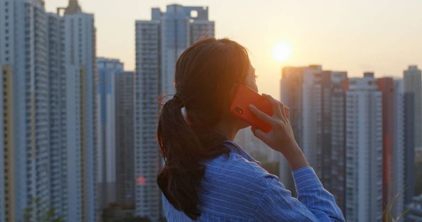 Жінка розмовляє з мобільним телефоном на задньому плані міста під час заходу сонця
 - Фото, зображення