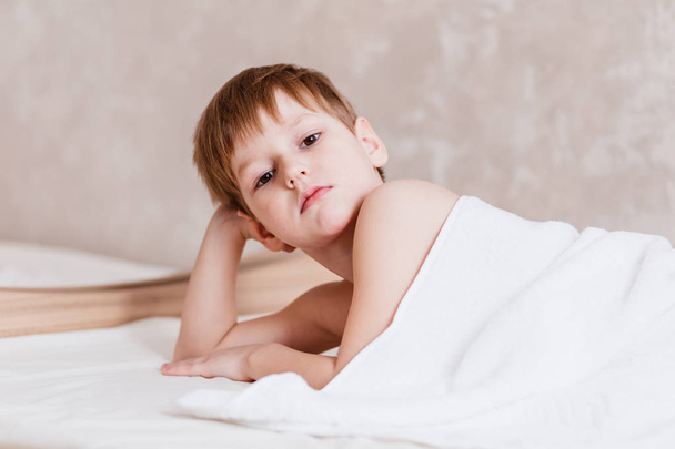 niño lindo caucasoide de cinco años cubierto con toalla Terry blanca en el dormitorio sobre fondo blanco
 - Foto, imagen