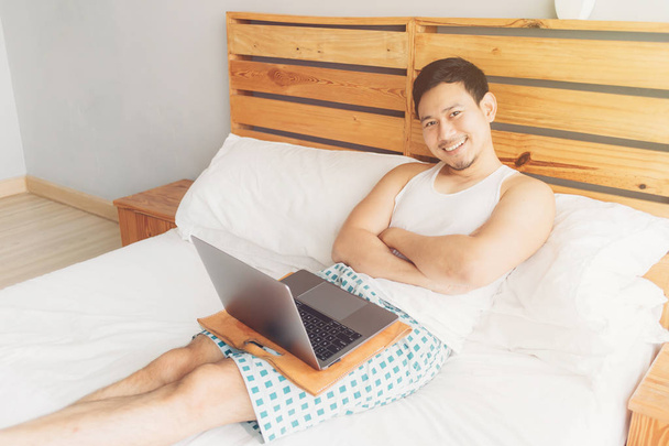 Happy man is working with his laptop on his bed. Concept of freelancer successful lifestyle. - Фото, зображення