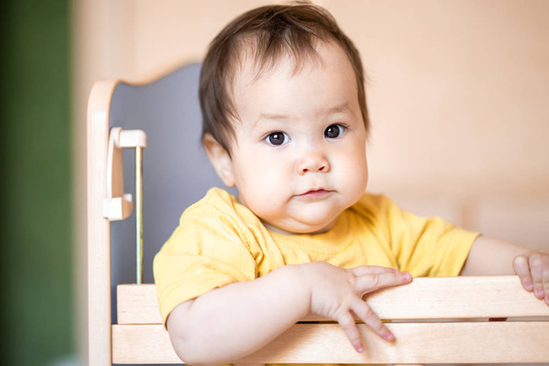 Sarı t-shirt evde beşik ayakta koyu saçlı sevimli küçük kız bebek - Fotoğraf, Görsel