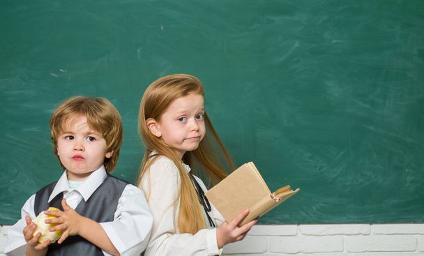 Funny little boy and cute little girl pointing up on blackboard. Copy space. Blackboard background. School kids. Kids from primary school. First school day. - Photo, Image