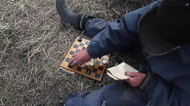Closeup of old hands playing checkers according to the scheme in a newspaper in nature, shepherd at work, selective focus - Footage, Video