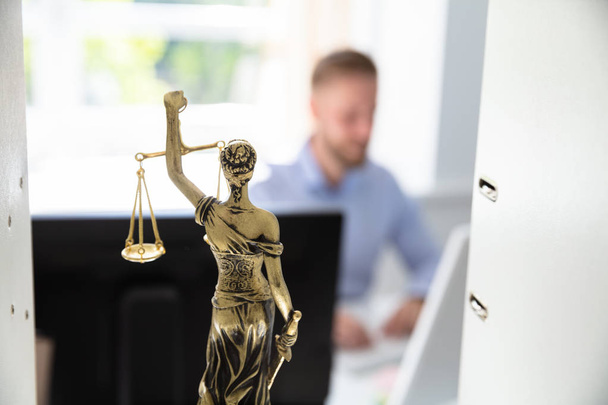 Άγαλμα δικαιοσύνης στο ράφι και δικηγόρος που εργάζεται στο γραφείο στο παρασκήνιο - Φωτογραφία, εικόνα