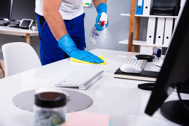 Janitor cleaning white desk in modern office - Foto, Imagen