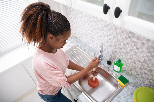 Side View Of A Female Plumber Using Plunger In Kitchen Sink - Photo, image