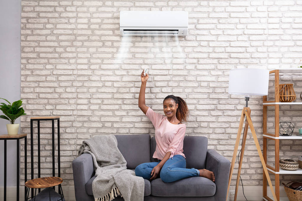 Young African Woman Switching On Air Conditioner With Remote Control At Home - Fotoğraf, Görsel