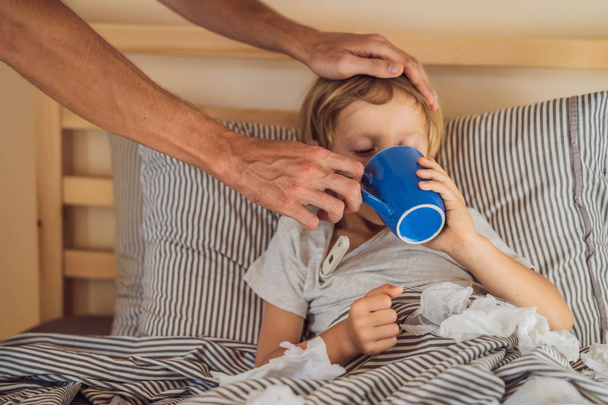 Больной мальчик пьет чай в своей постели. Больной ребенок с температурой и болезнью в постели
 - Фото, изображение