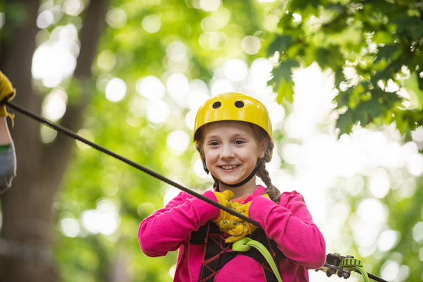 Happy little child climbing on a rope playground outdoor. Cute child in climbing safety equipment in a tree house or in a rope park climbs the rope. Toddler kindergarten. - Foto, Imagen
