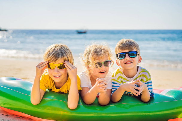 Children sit on an inflatable mattress in sunglasses against the sea and have fun - Foto, immagini
