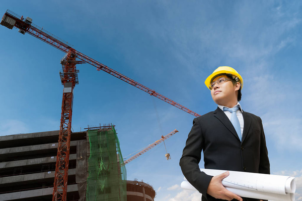 Ingénieur tenant le plan dans sa main sur le chantier de construction avec fond de machine de grue
 - Photo, image