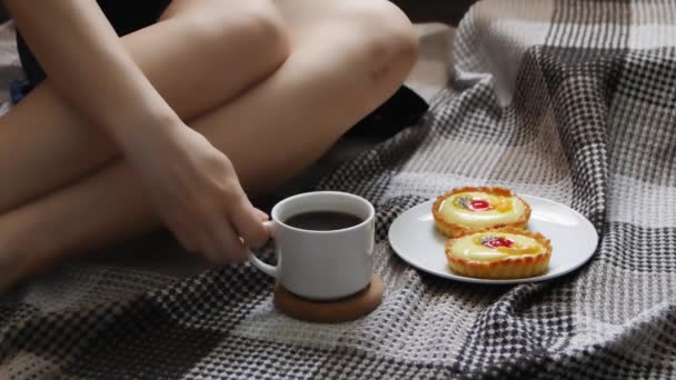 女の子はベッドで朝のコーヒーとケーキで目を覚ます。居心地の良い青いローブでベッドでコーヒーを飲む美しい若い女性. - 映像、動画