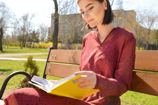 Kaunis nuori nainen lukee kirjaa penkillä puistossa
 - Valokuva, kuva