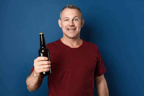 色の背景にビールのボトルを持つ幸せな中年の男 - 写真・画像