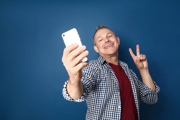 Szczęśliwy mężczyzna w średnim wieku, biorąc selfie na kolorowym tle - Zdjęcie, obraz