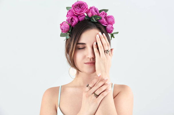 Young woman with beautiful flowers on her head on light background - Фото, изображение