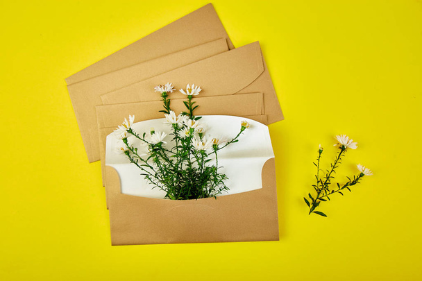 Zlatá obálka s uspořádáním jarní květiny na žlutém pozadí. Plochý, pohled shora. Otevřeli obálku. Slavnostní pozdrav - Fotografie, Obrázek