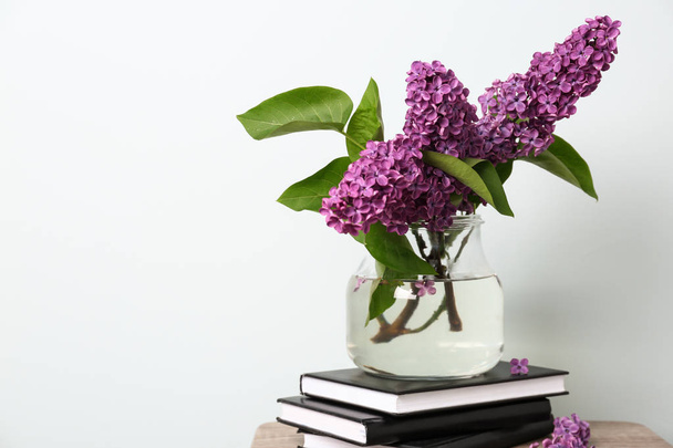 Beautiful lilac flowers in vase with books on table against light background - Fotografie, Obrázek