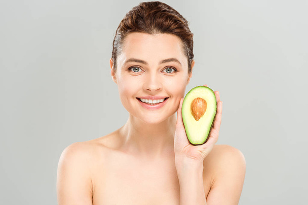 cheerful naked woman holding half of organic and ripe avocado isolated on grey  - Fotó, kép