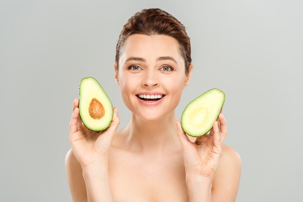 happy naked woman holding halves of organic avocado isolated on grey  - Fotó, kép