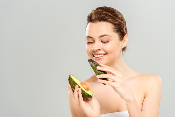 happy woman holding halves of organic avocado isolated on grey  - Фото, зображення
