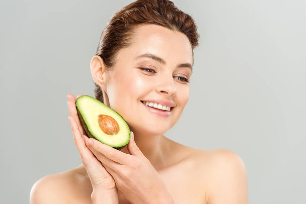 happy and naked woman holding half of ripe avocado isolated on grey  - Photo, Image