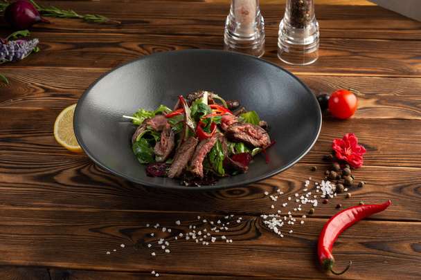 Thai beef salad in black plate on wooden background - Photo, image