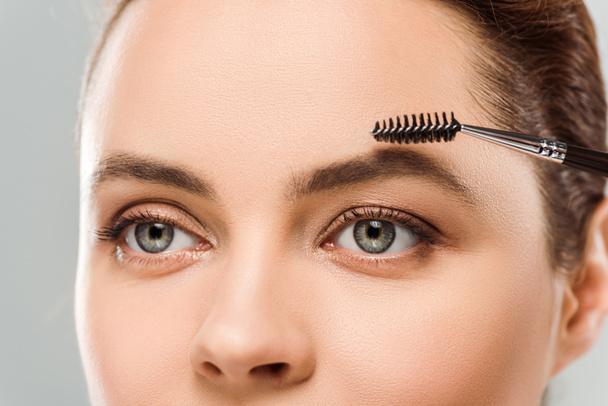 abgeschnittene Ansicht der Frau Gestaltung Augenbraue mit Augenbrauenbürste isoliert auf grau - Foto, Bild
