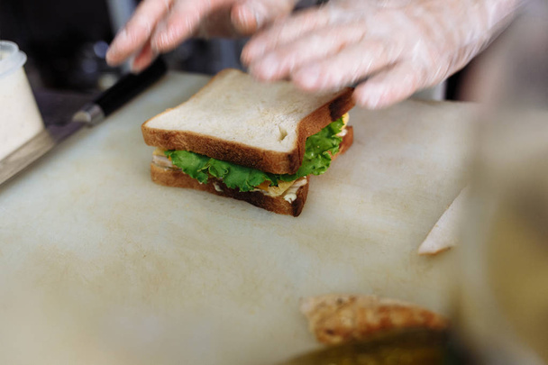 cook in polyethylene gloves making a sandwich on a white board - Foto, Bild