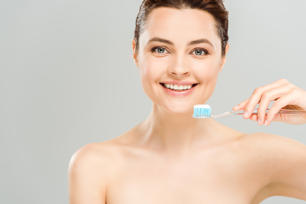 vidám meztelen nő mosolyogva, miközben fogkefét a fogkrém izolált szürke  - Fotó, kép