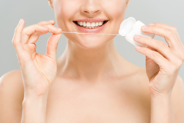 обрезанный вид веселой голой женщины, держащей зубную нить рядом с зубами, изолированными на сером
  - Фото, изображение