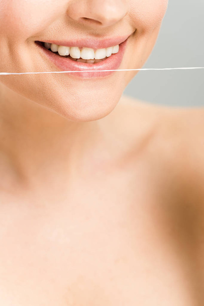 przycięte widok szczęśliwy nagi kobieta trzyma dentystyczne nici w pobliżu zębów na szarym tle  - Zdjęcie, obraz