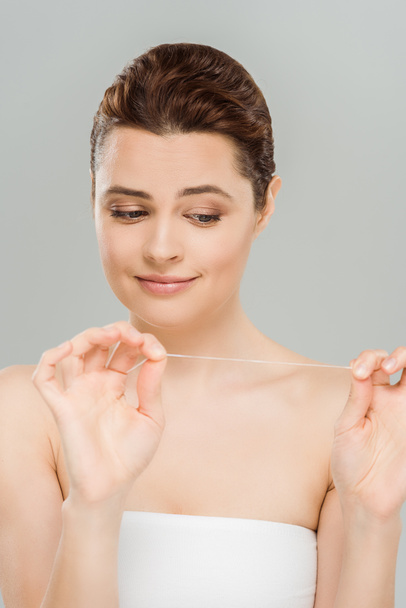 attractive woman looking at dental floss isolated on grey  - Fotografie, Obrázek