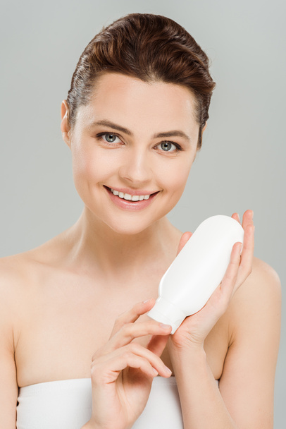 happy woman holding bottle of body lotion isolated on grey  - Foto, imagen