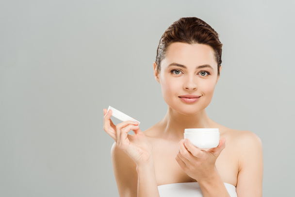 positive woman holding container with cosmetic cream isolated on grey  - Foto, immagini