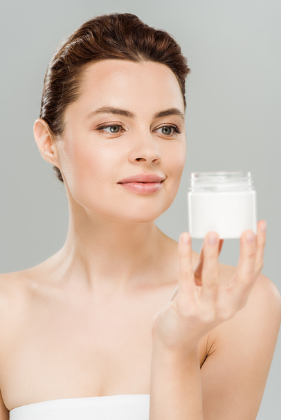 happy woman looking at container with cosmetic cream isolated on grey  - Photo, Image